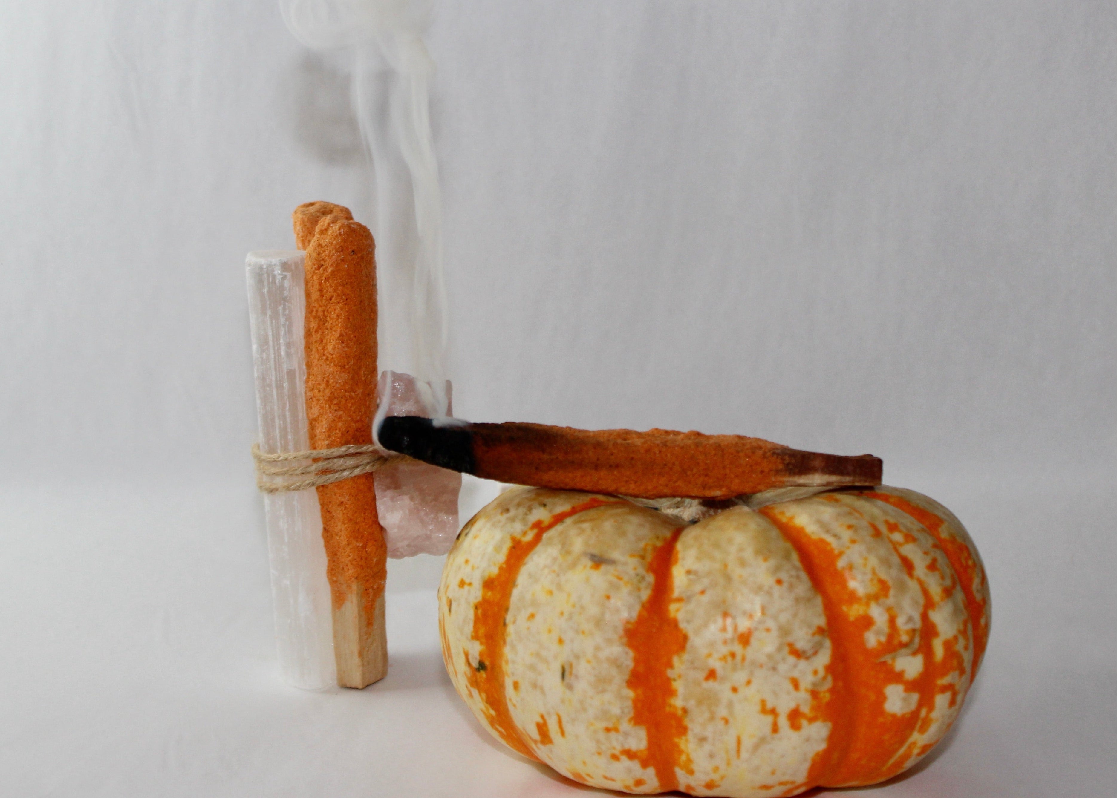 Pumpkin spice palo santo bundle with rose quartz and selenite tied together in twine beside a mini pumpkin, smoke rising  autumn cleansing ritual aesthetic by DeadNova.