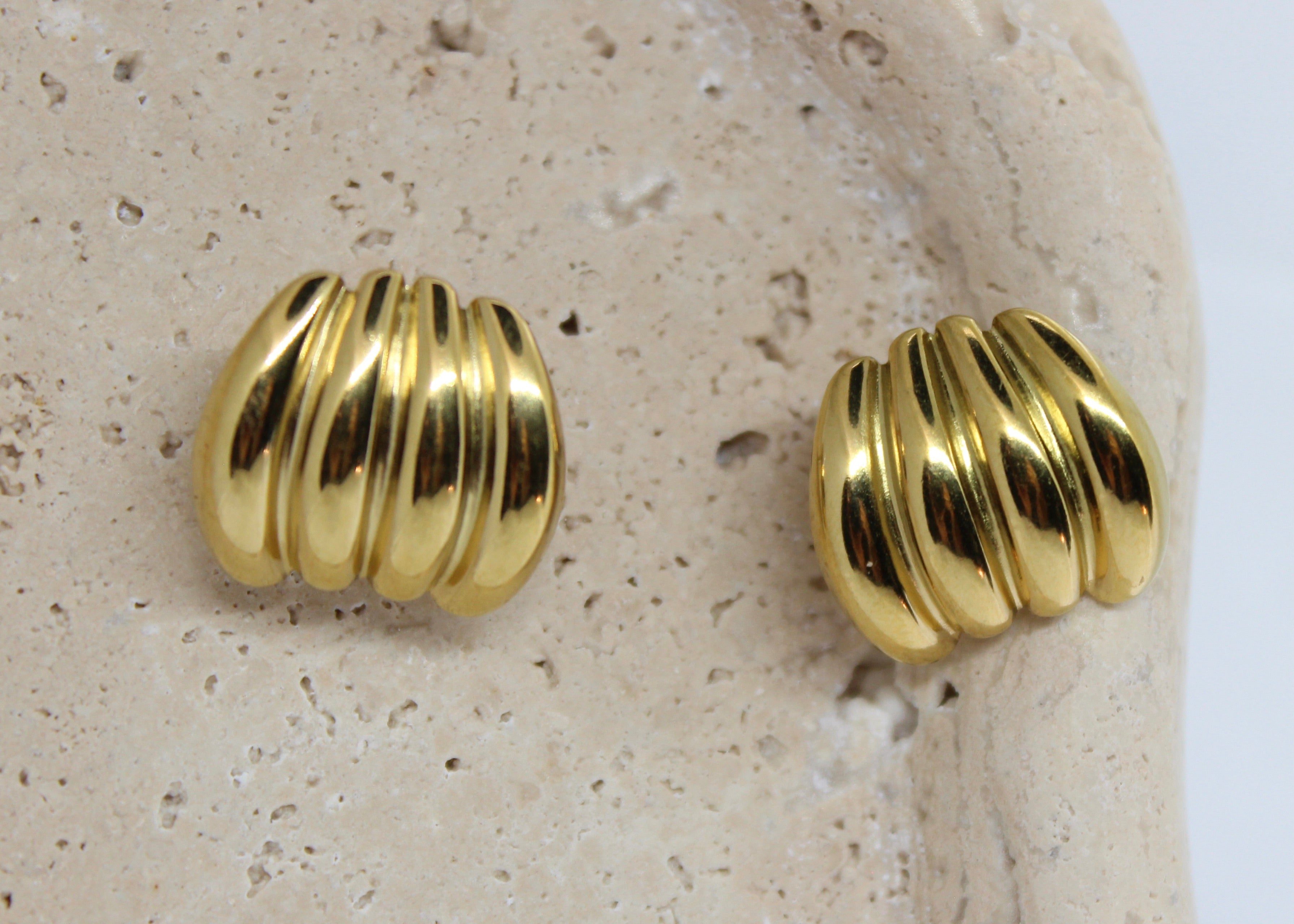 Pair of gold ribbed earrings on a textured beige surface